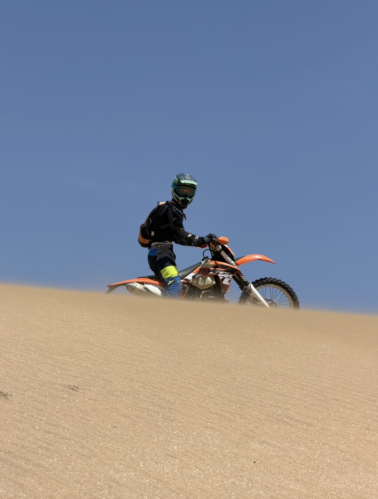 Pilote enduro sur crête de dune sous ciel bleu — Agadir, Maroc